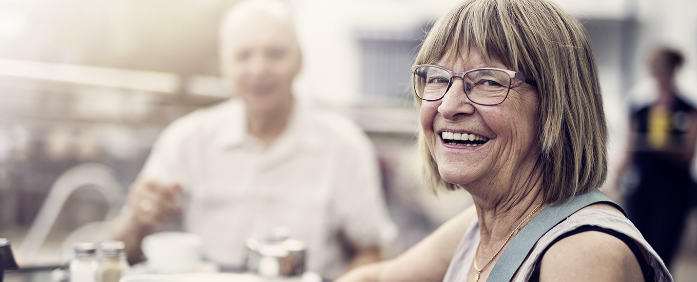 Elderly woman smiling with elderly man in background