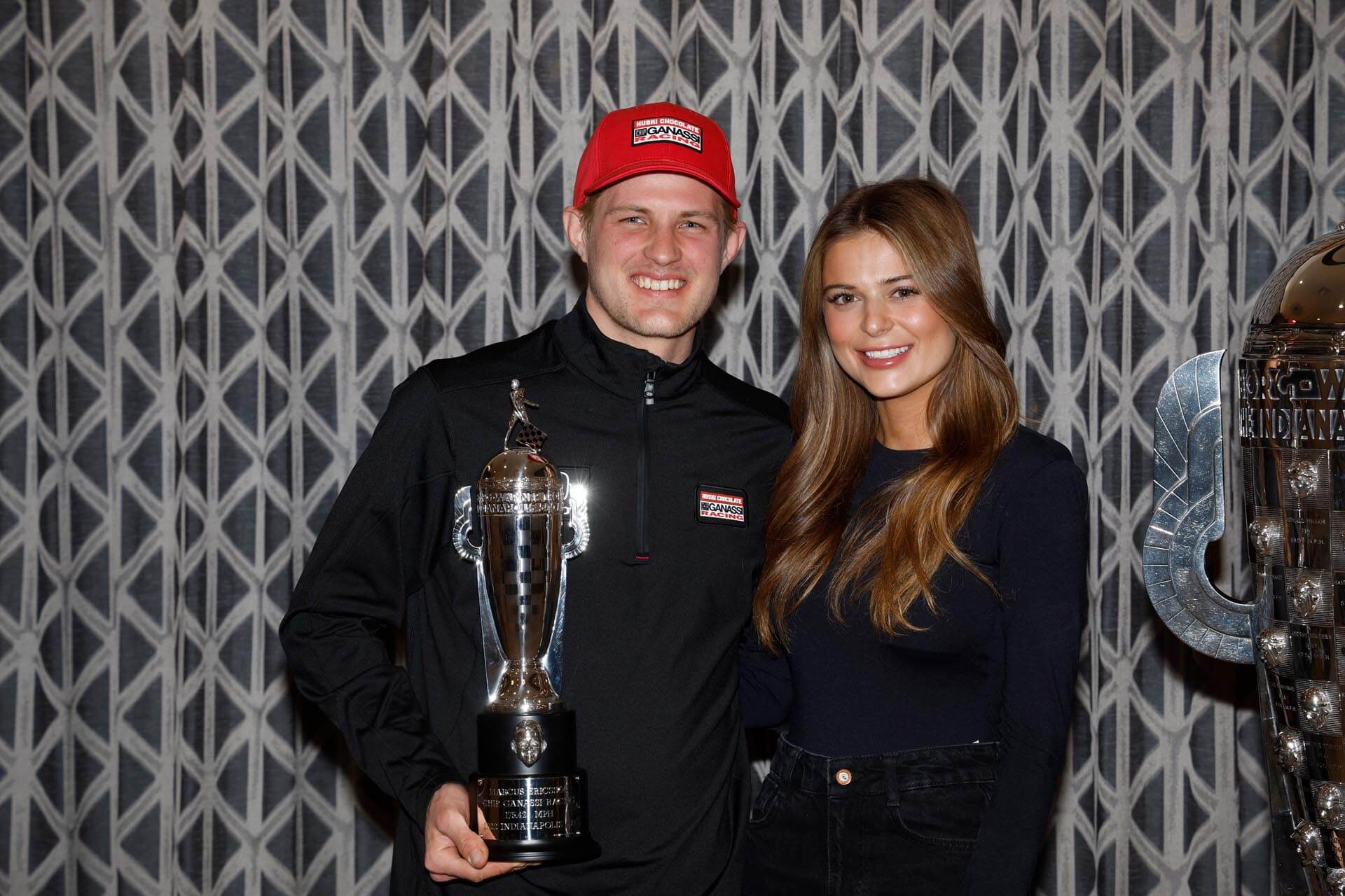 Smiling man and woman stand with man holding trophy