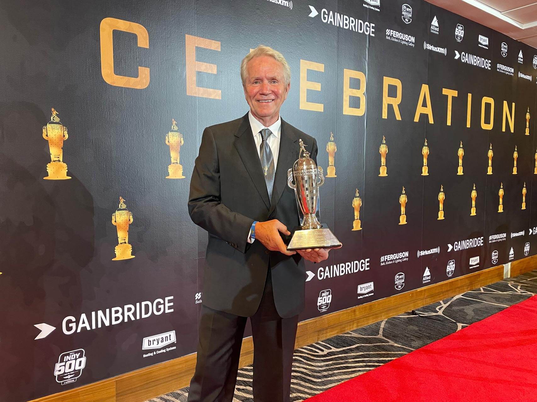 Man in suit holds silver trophy