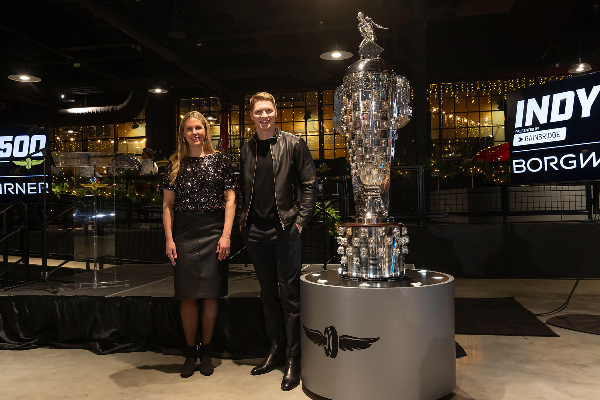 Woman and man stand next to large silver trophy