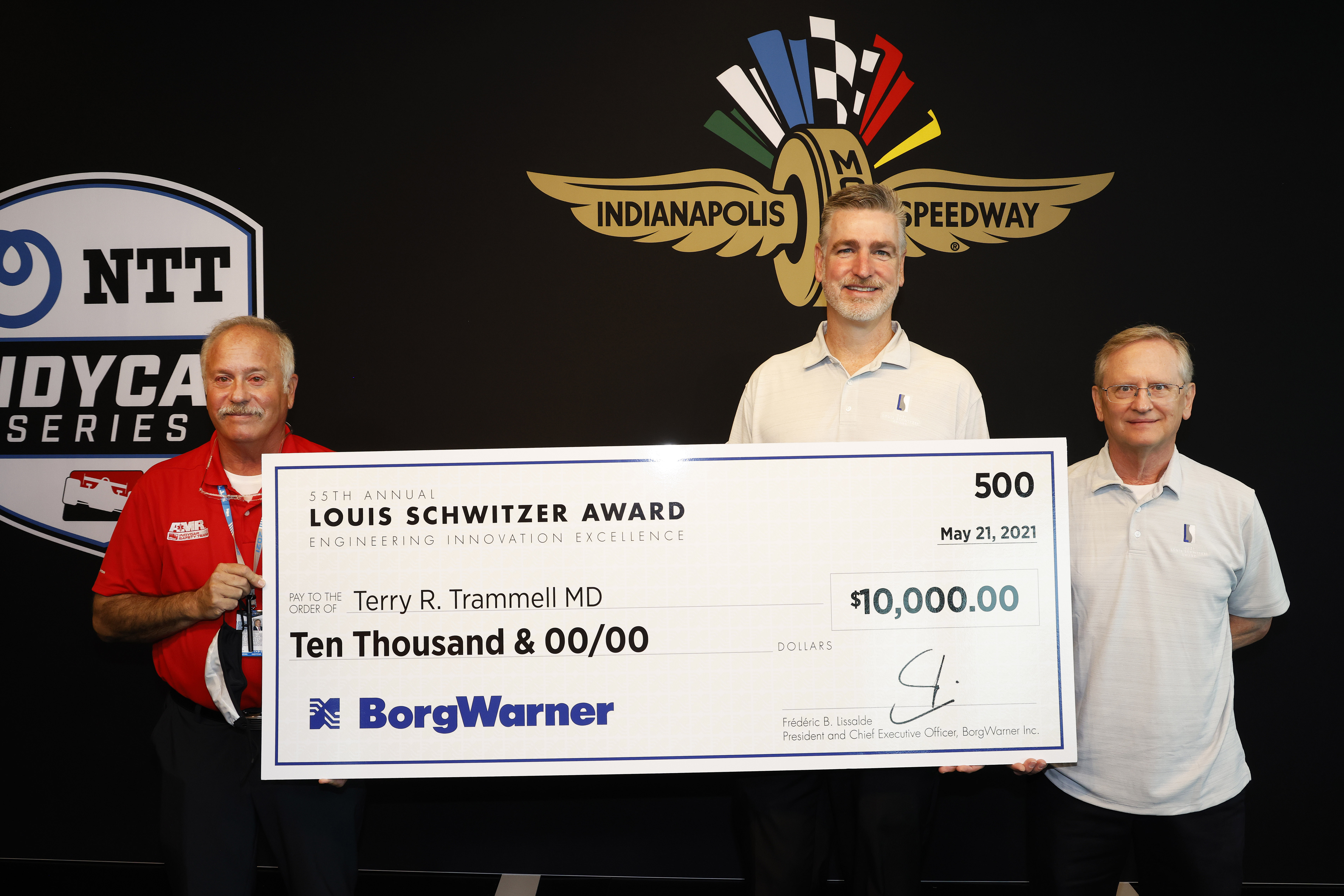 Three men hold large check against black logo backdrop