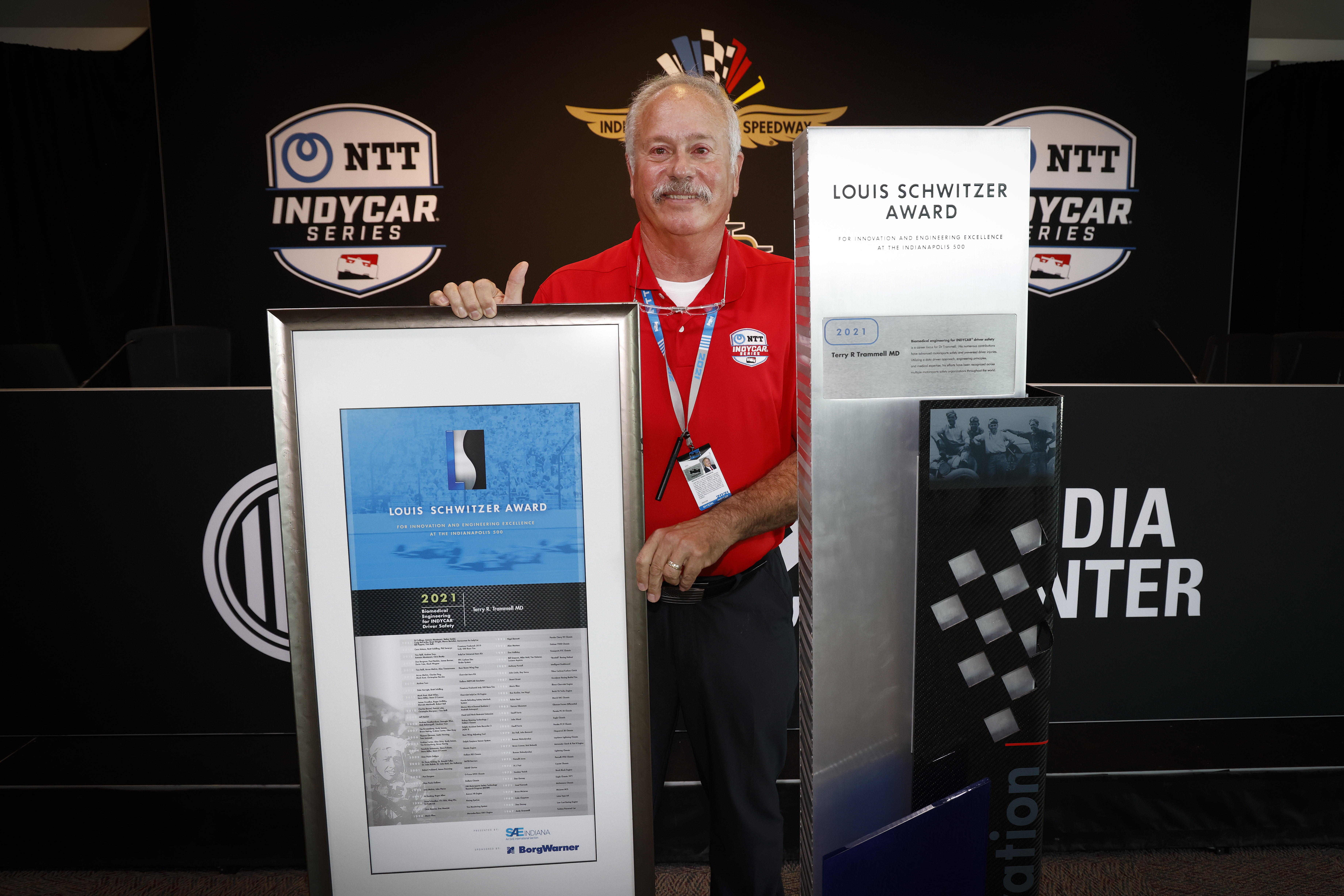 Man stands with large plaque against black logo backdrop