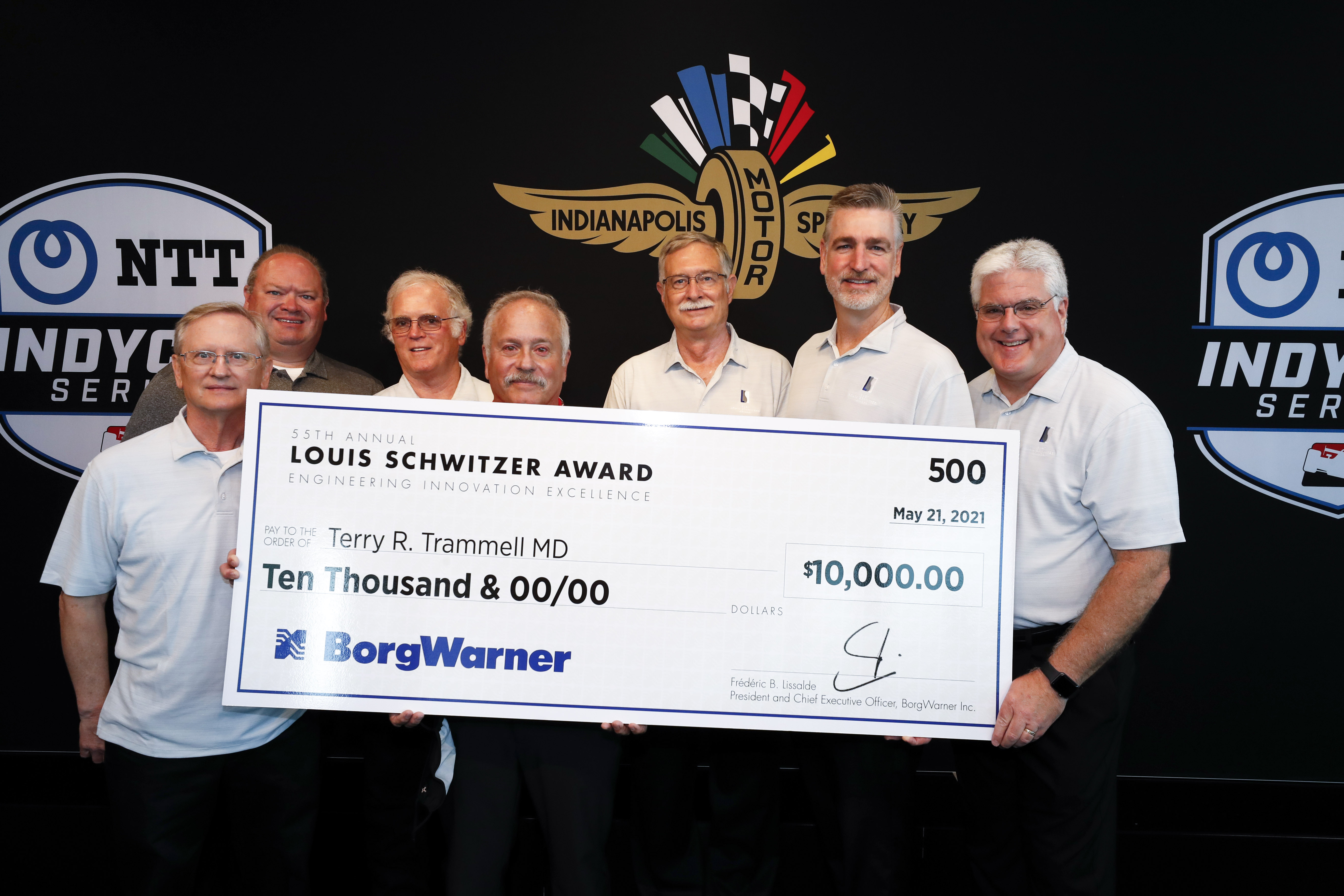 Seven men hold large check against black logo backdrop