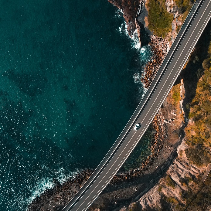 Aerial view of white car driving along coastal bridge